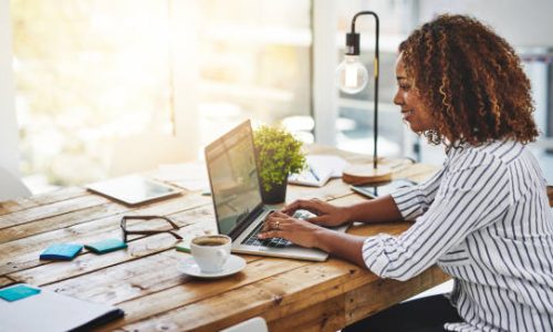 Cropped shot of a woman using her laptop on a wooden table
